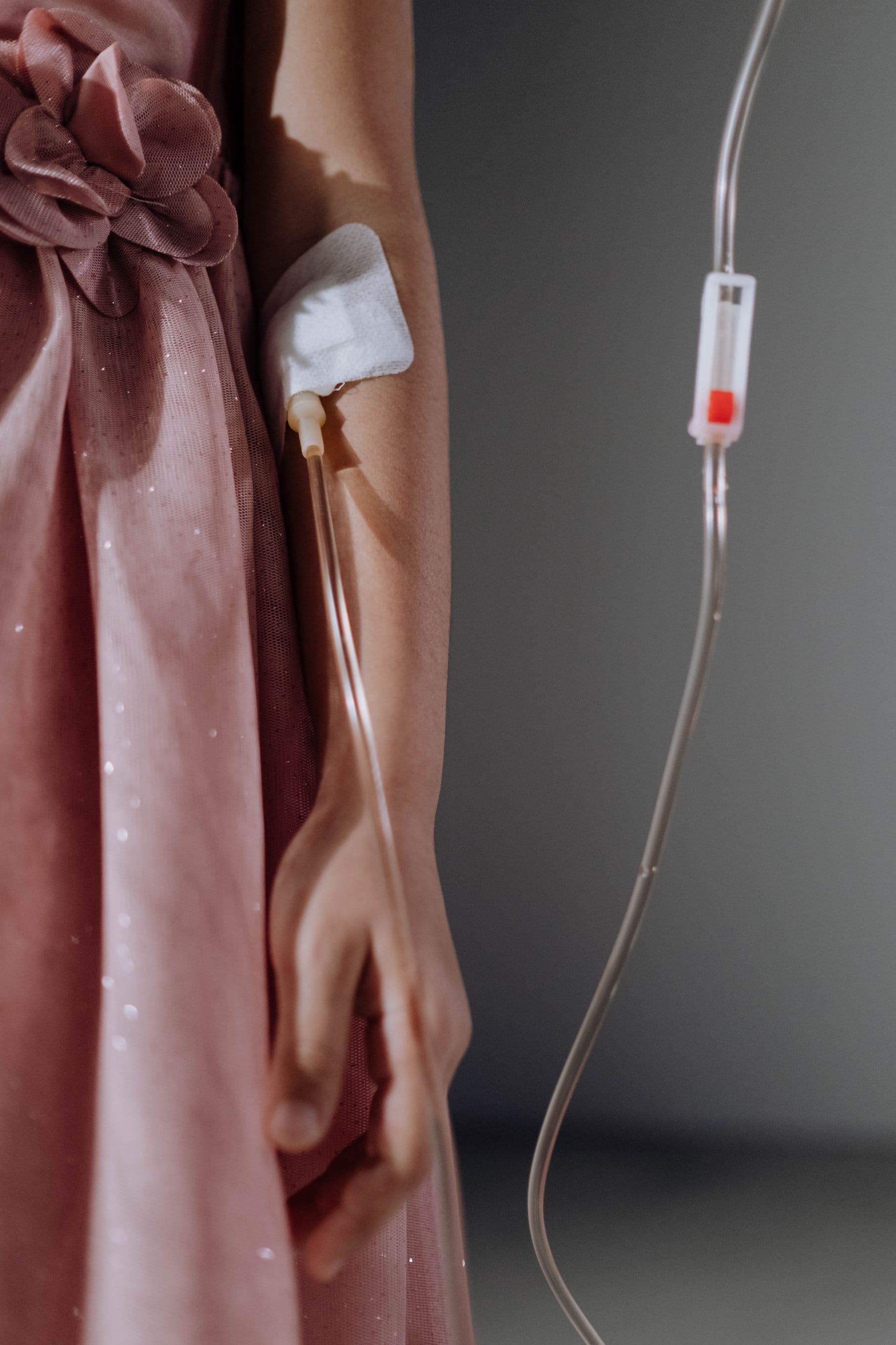 Close-up of a woman in a pink dress receiving IV therapy, the line taped neatly to her arm.
